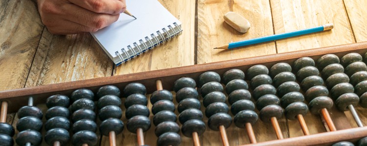 person with pencil and notebook counting on abacus