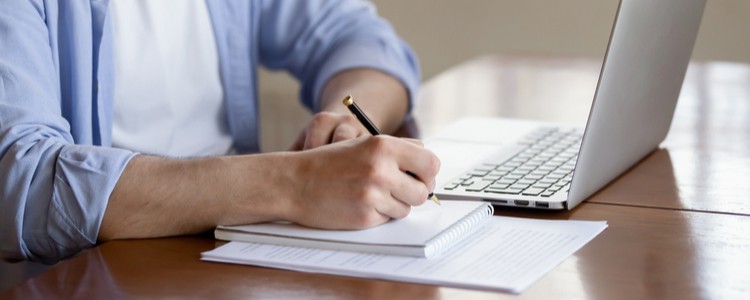 male student making notes while watching laptop screen