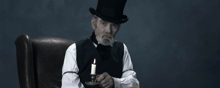 man dressed as Ebenezer Scrooge sitting in a chair holding a candle